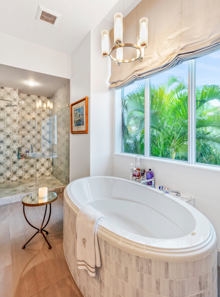 Tiled oval bathtub inside a white bathroom with a cream-tiled shower room